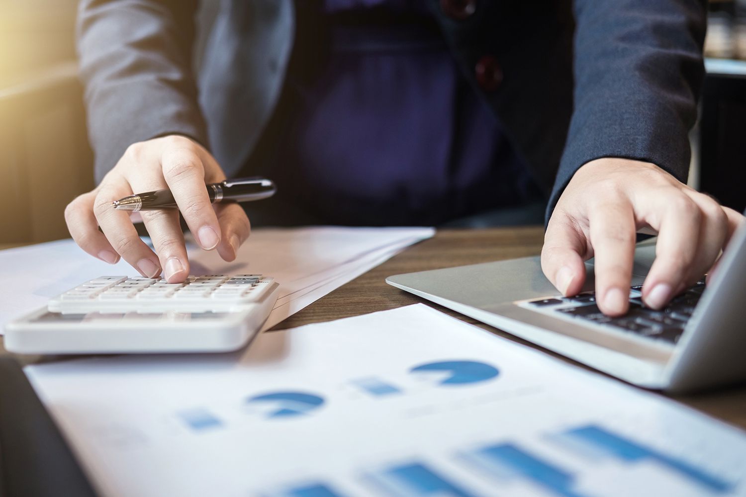 Midsection of Businessman Using Calculator and Laptop at Desk