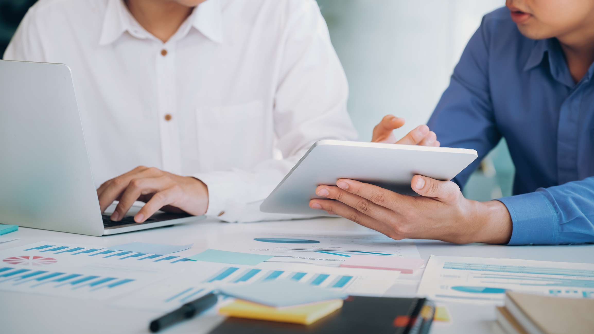 midsection of businessmen working on laptops with graphs and charts on the table around them