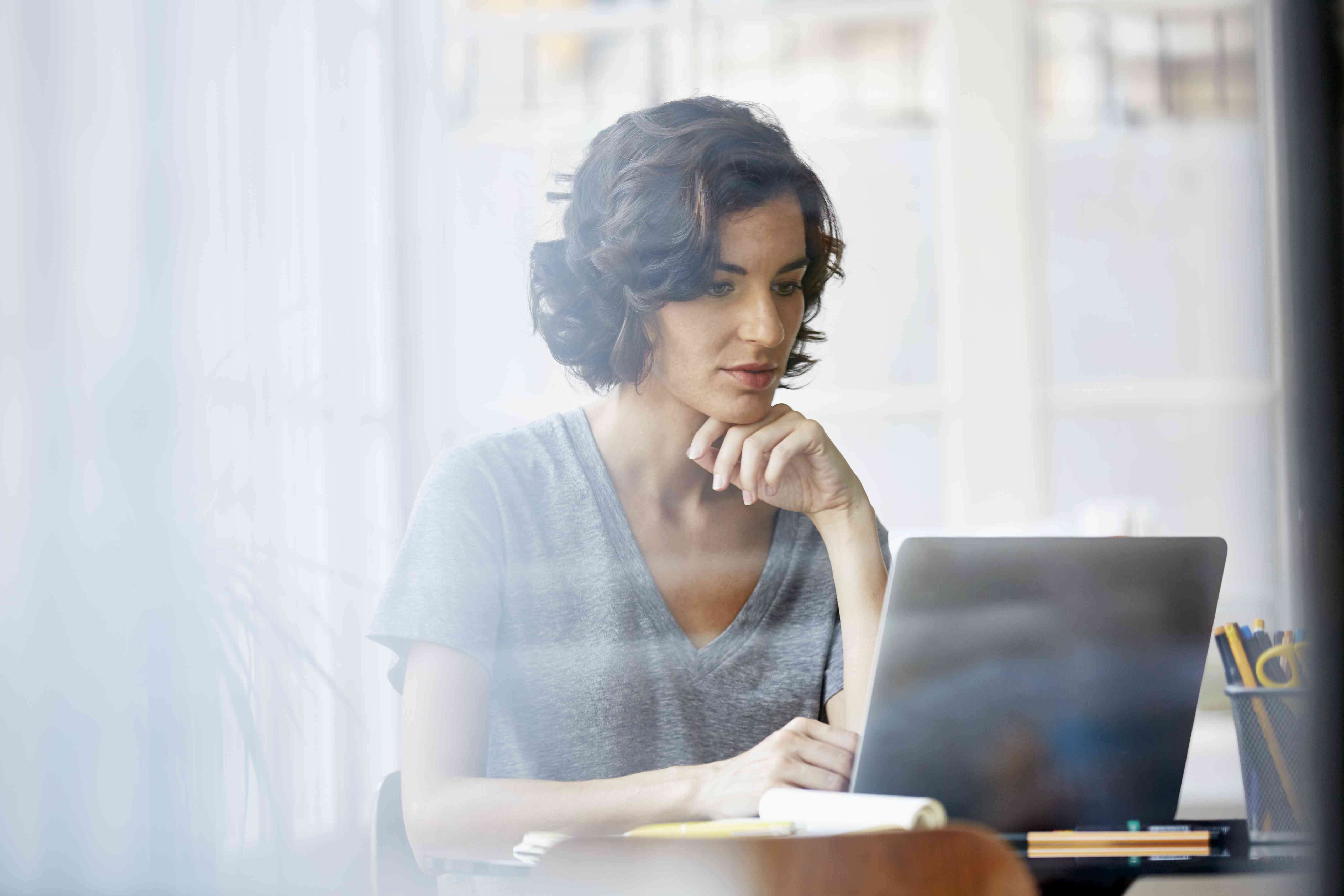 Young white woman with hand on chin at a laptop in an office