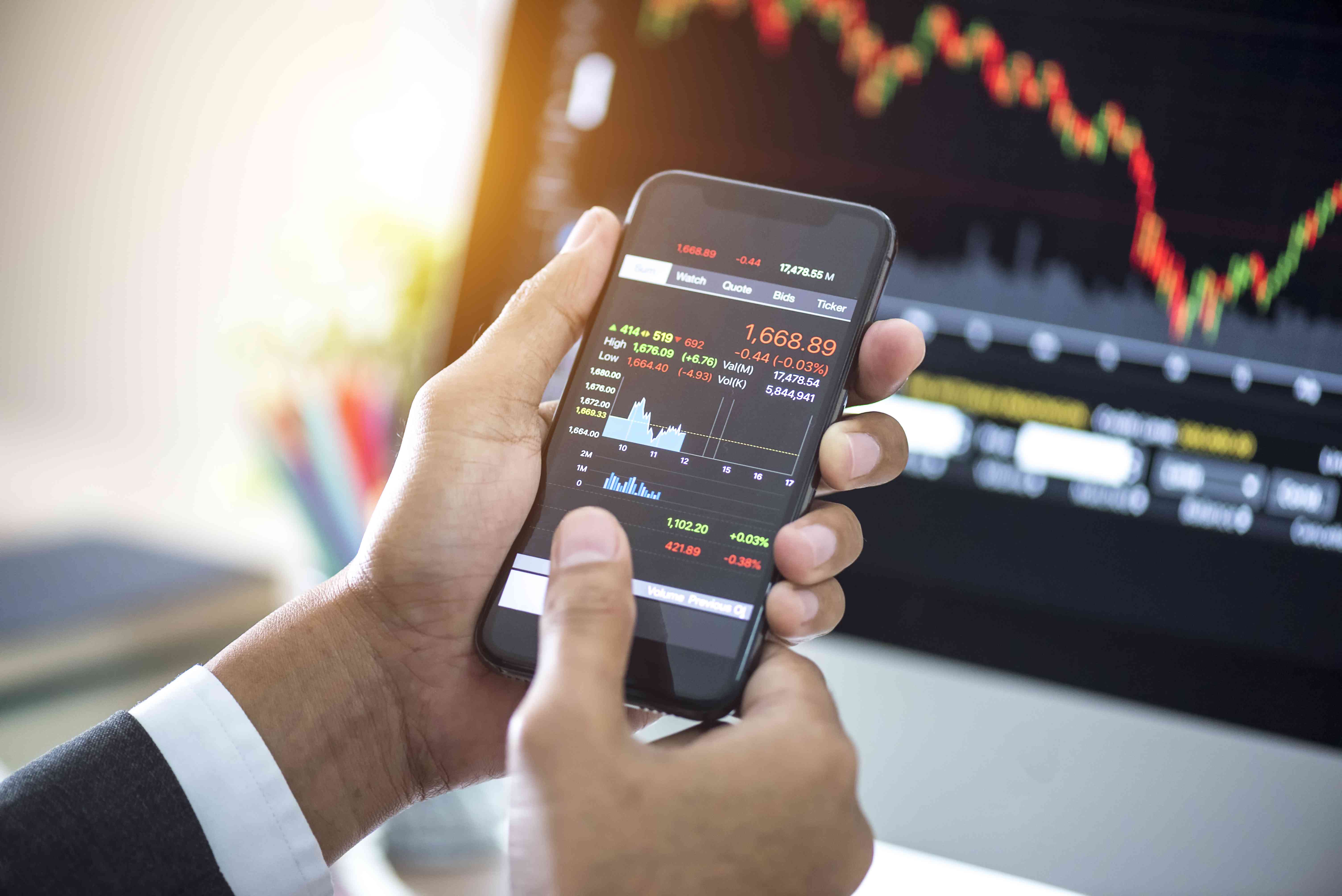 Investor analyzing stock market investments with financial dashboard on smartphone and computer screens